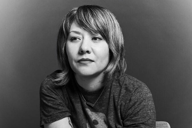 A woman with short hair and lipstick gazes away from the camera for a photo