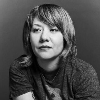 A woman with short hair and lipstick gazes away from the camera for a photo