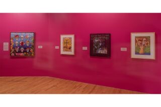 A collection of artworks hang on the wall of a pink gallery space.