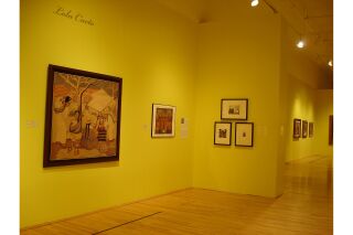 Highlights two walls featuring Cueto’s work. Left wall shows two textile pieces and artist description. Right wall shows three black and white etchings