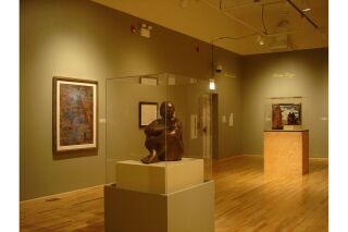 Two gallery walls visible with two sculptures encased in glass in center of gallery. Two paintings along left wall and one painting on right wall