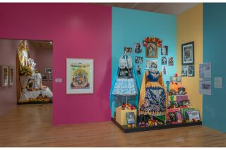 A colorful Serigraph depicting an Ofrenda next to an Altar displaying blue children's dresses, photographics, flowers and papeles picados.
