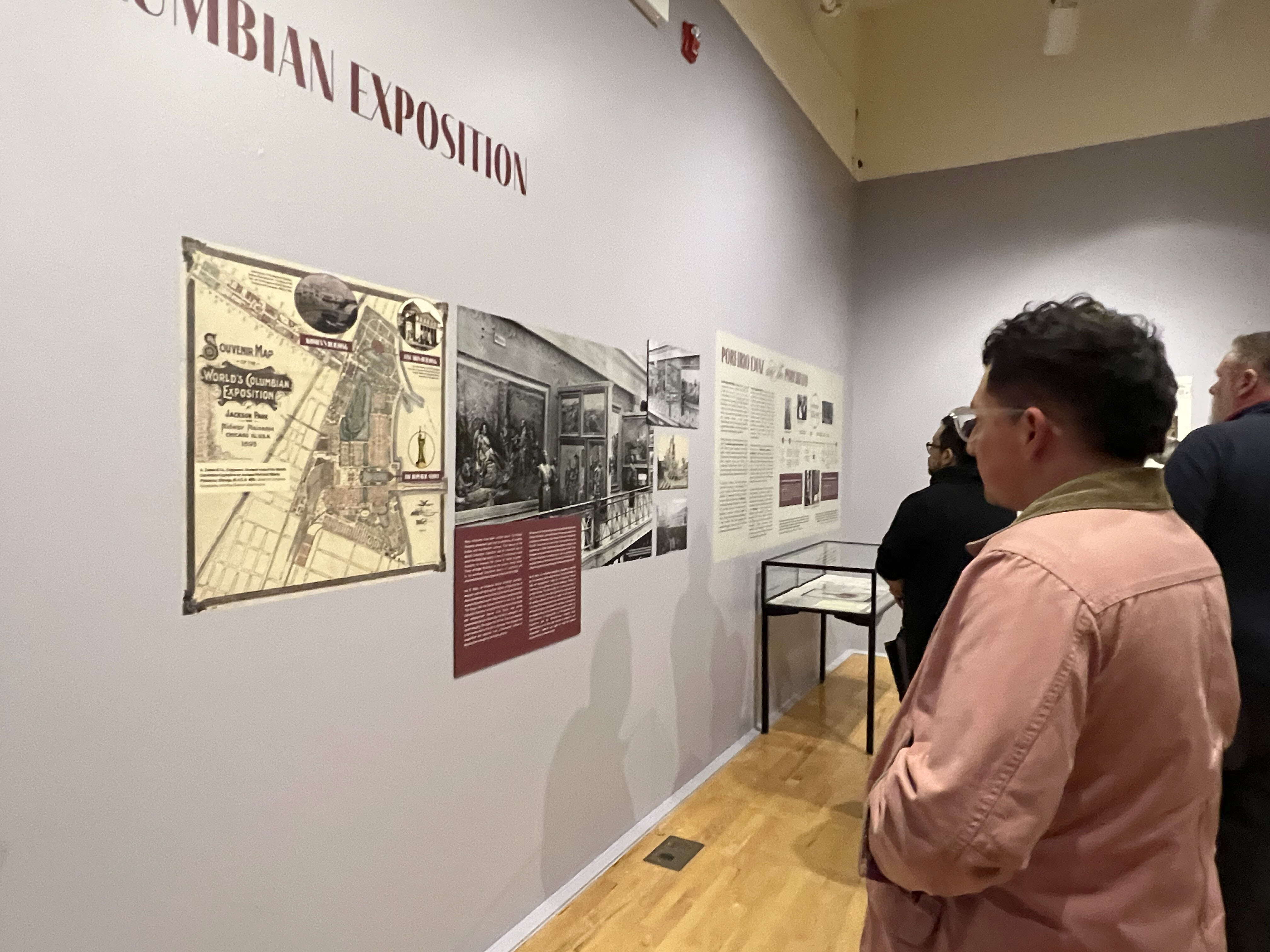 A person in a pink jacket reads wall text about the exhibition.
