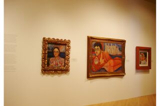 Image of gallery wall with exhibit description cut off on left side and three paintings to the right