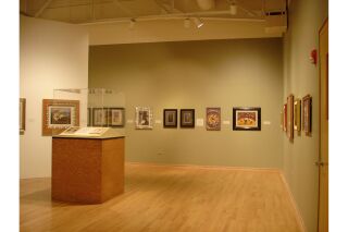 Image of three gallery walls and podium with glass case in the center of the room