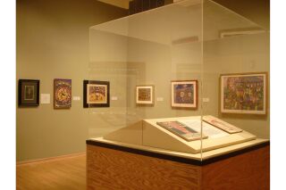 Gallery image of glass-encased art on podium in center of room and two gallery walls