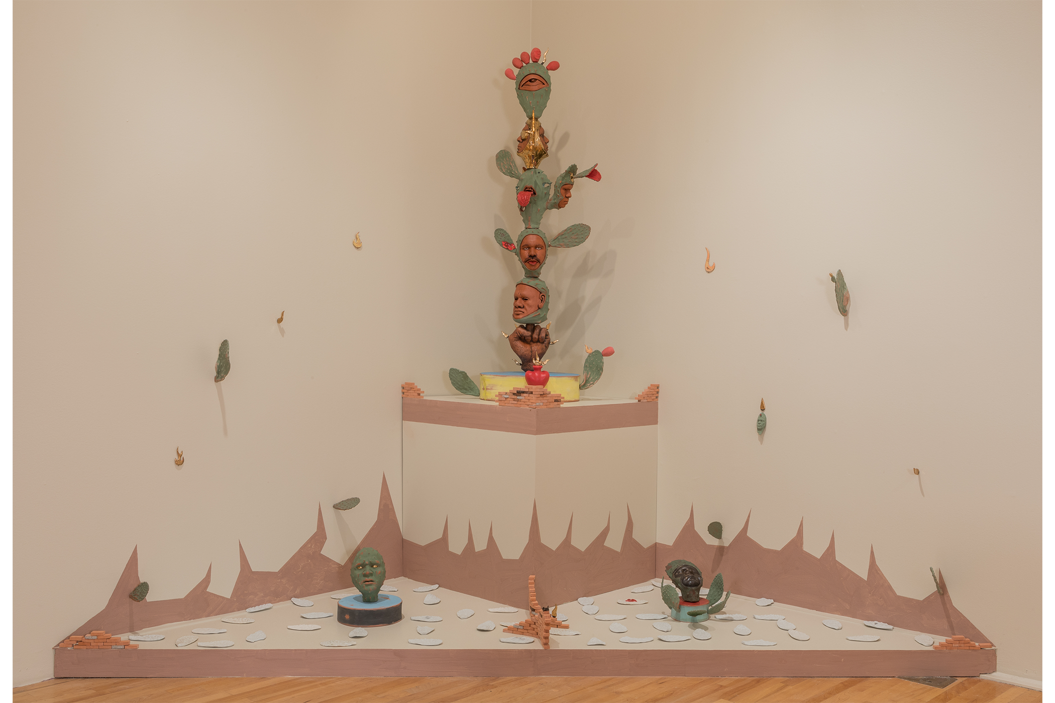 installation of artwork in the corner, sculpture depicts cacti with human heads and parts coming out of the cactus pieces.